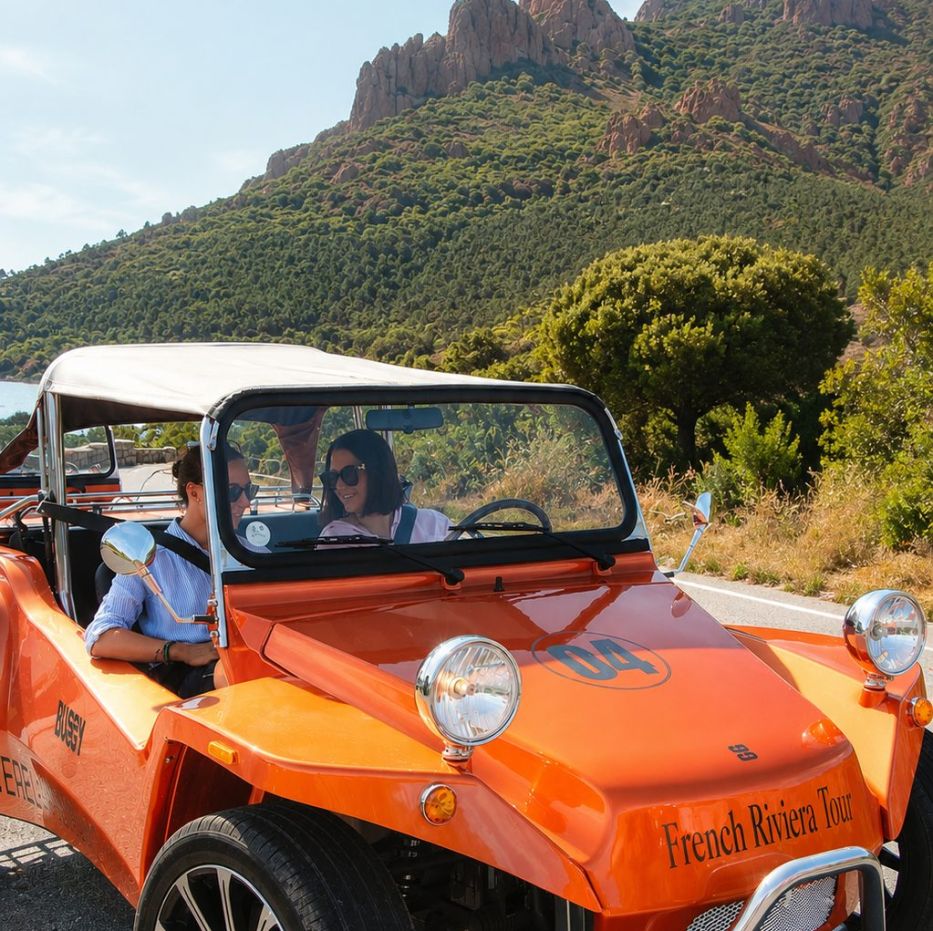 Couple au volant d’un buggy vintage orange devant les roches rouges de l’Estérel